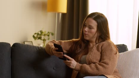 Woman-Sitting-On-Sofa-At-Home-Using-Mobile-Phone-To-Check-Social-Media-Message-And-Scrolling-Online-11